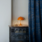 The orange Panthella 250 Portable Lamp from Louis Poulsen in a primary bedroom on top of a side table.