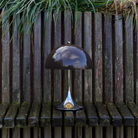 The 13.2 inch brown Panthella Portable Lamp: The Originals from Louis Poulsen in a garden on top of a bench.