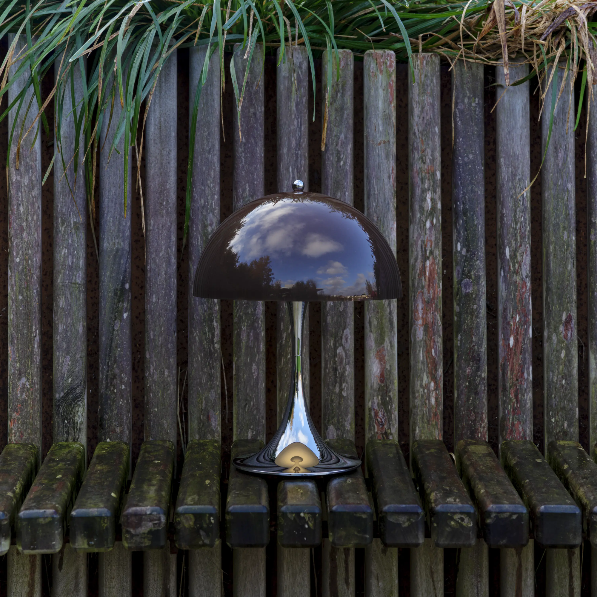The 13.2 inch brown Panthella Portable Lamp: The Originals from Louis Poulsen in a garden on top of a bench.
