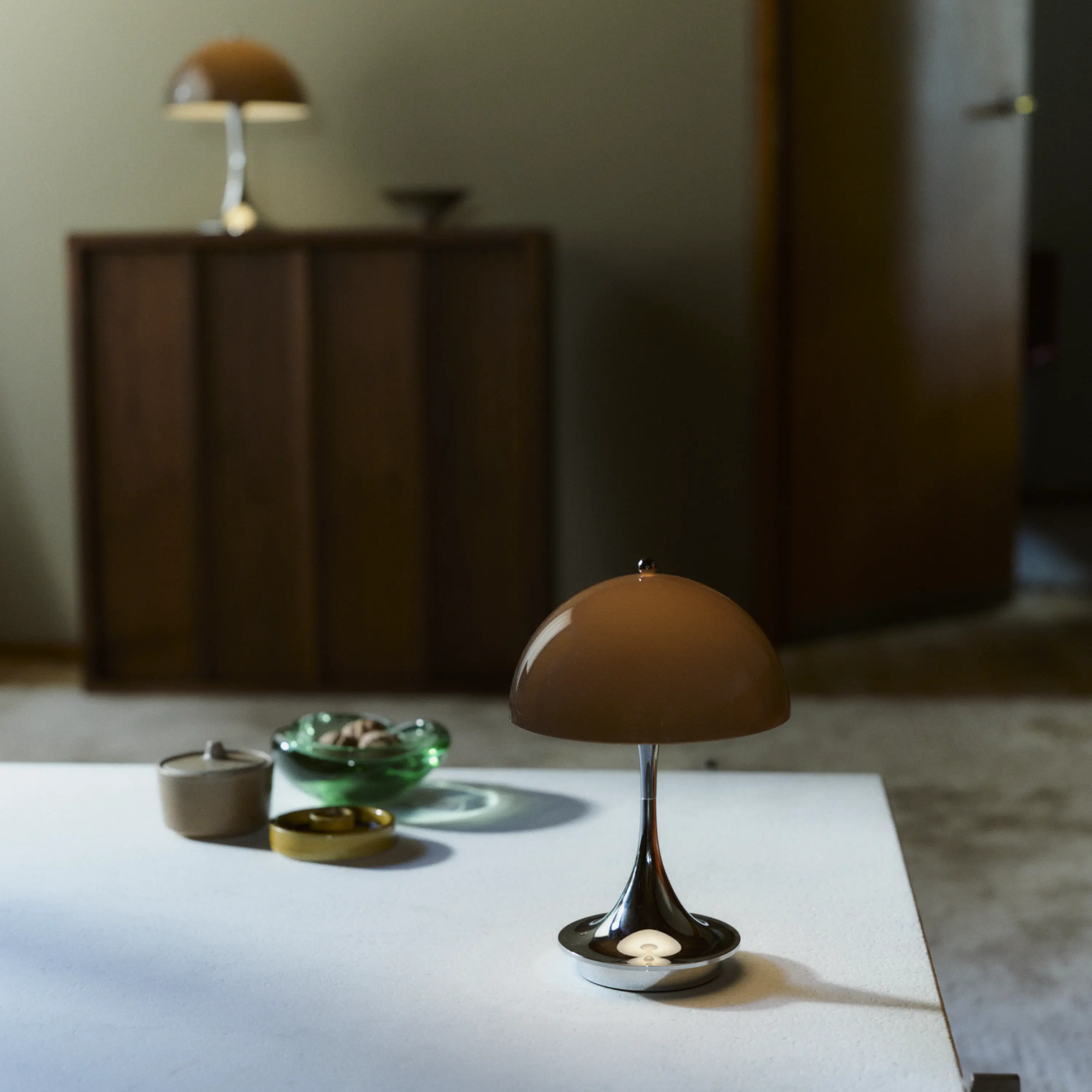 The 9.5 inch brown Panthella Portable Lamp: The Originals from Louis Poulsen on top of a table in a family area beside various trays.