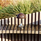 The 9.5 inch brown Panthella Portable Lamp: The Originals from Louis Poulsen in a garden on a bench.