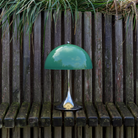 The 13.2 inch green Panthella Portable Lamp: The Originals from Louis Poulsen in a garden on top of a bench.