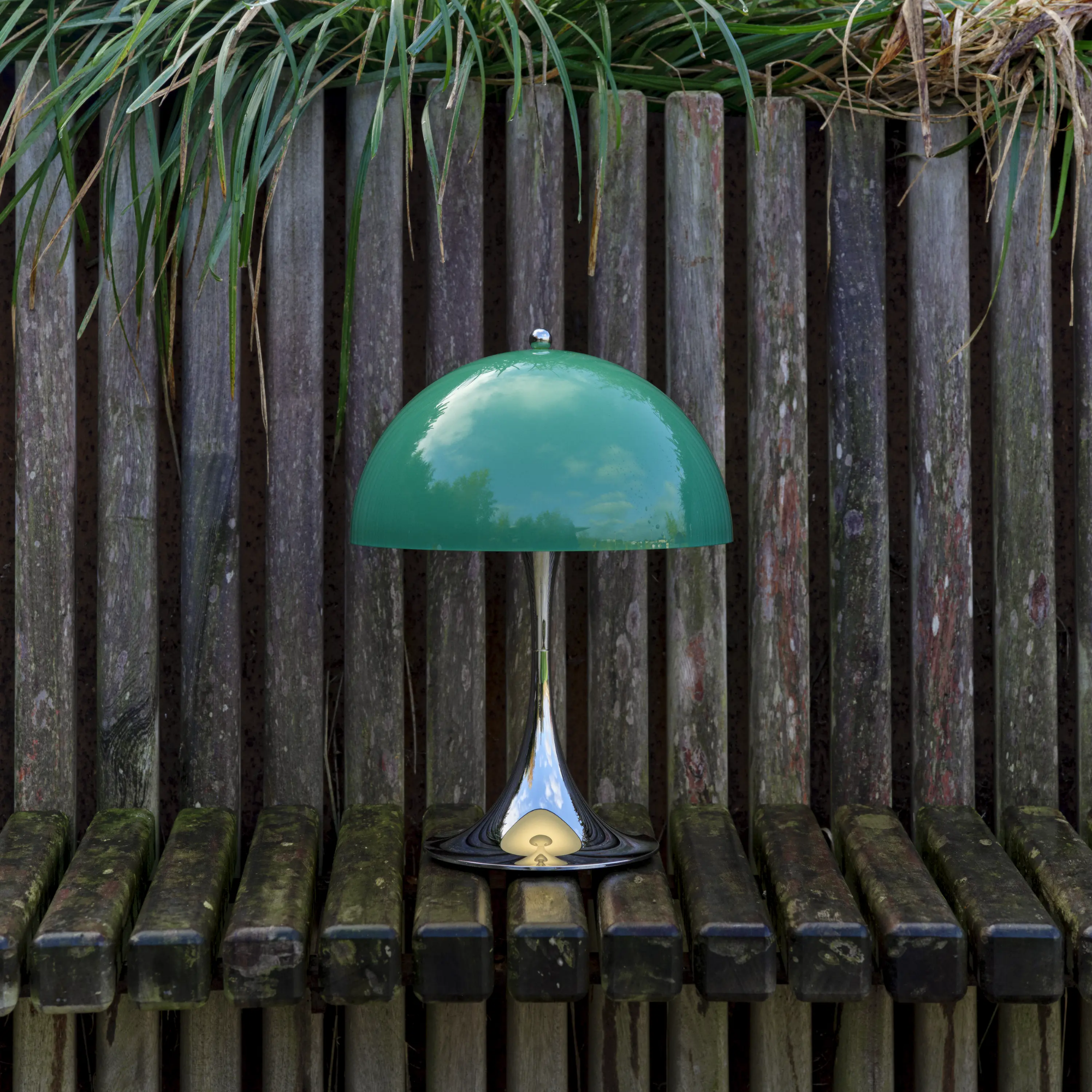 The 13.2 inch green Panthella Portable Lamp: The Originals from Louis Poulsen in a garden on top of a bench.