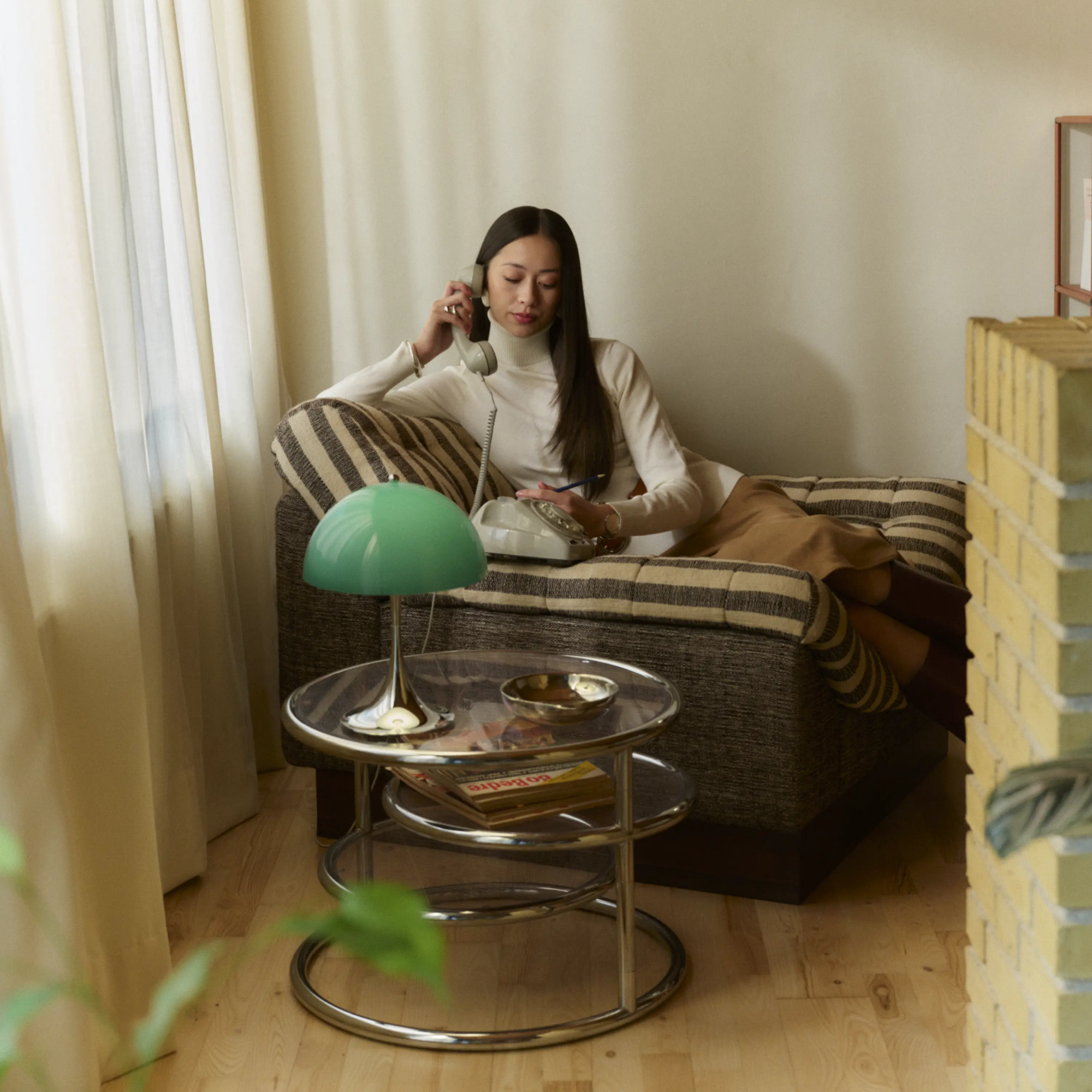 The 13.2 inch green Panthella Portable Lamp: The Originals from Louis Poulsen in a lounge next to a woman on a lounge chair using a phone.