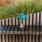 The 9.5 inch green Panthella Portable Lamp: The Originals from Louis Poulsen in a garden beside various plants.