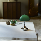 The 9.5 inch green Panthella Portable Lamp: The Originals from Louis Poulsen in a living room on top of a marble coffee table.