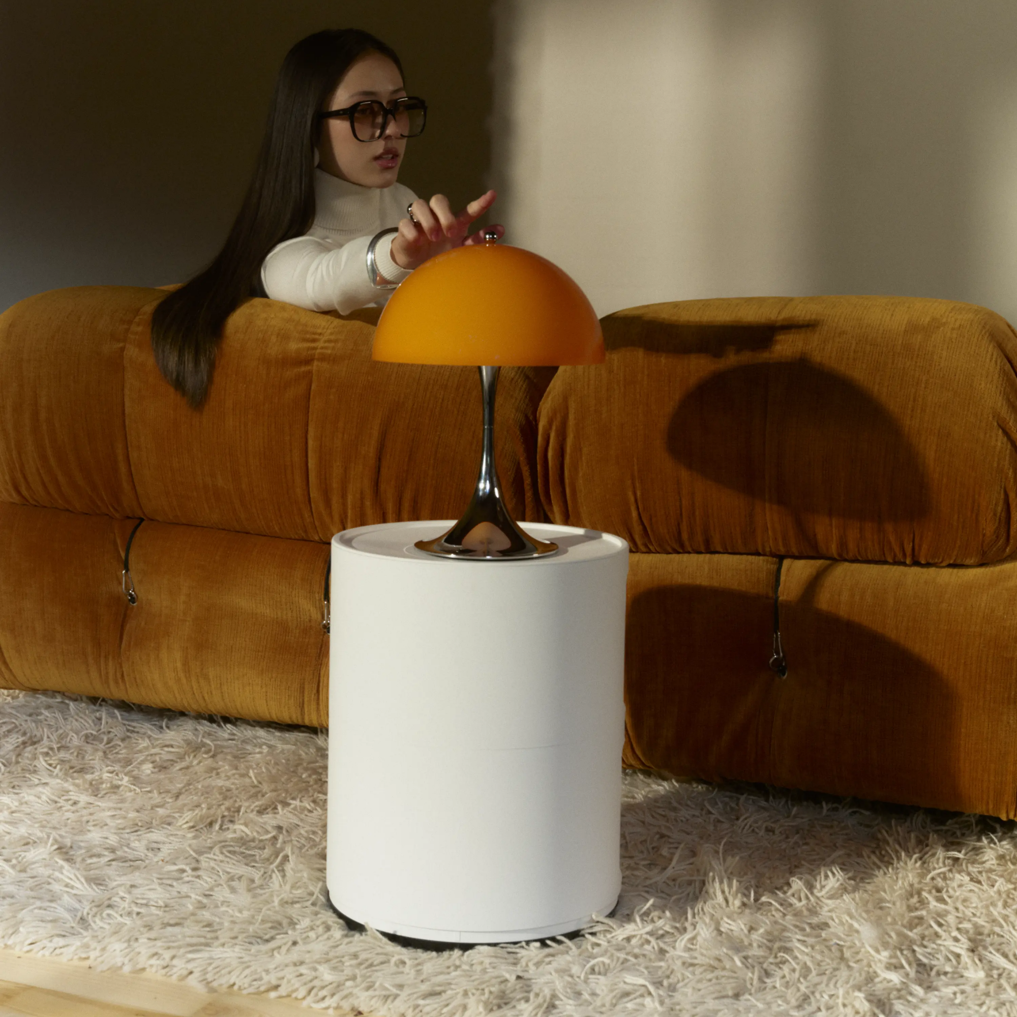 The 13.2 inch orange Panthella Portable Lamp: The Originals from Louis Poulsen in a family area being used by a woman on a couch.