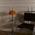 The 13.2 inch orange Panthella Portable Lamp: The Originals from Louis Poulsen in a living room next to a chair.