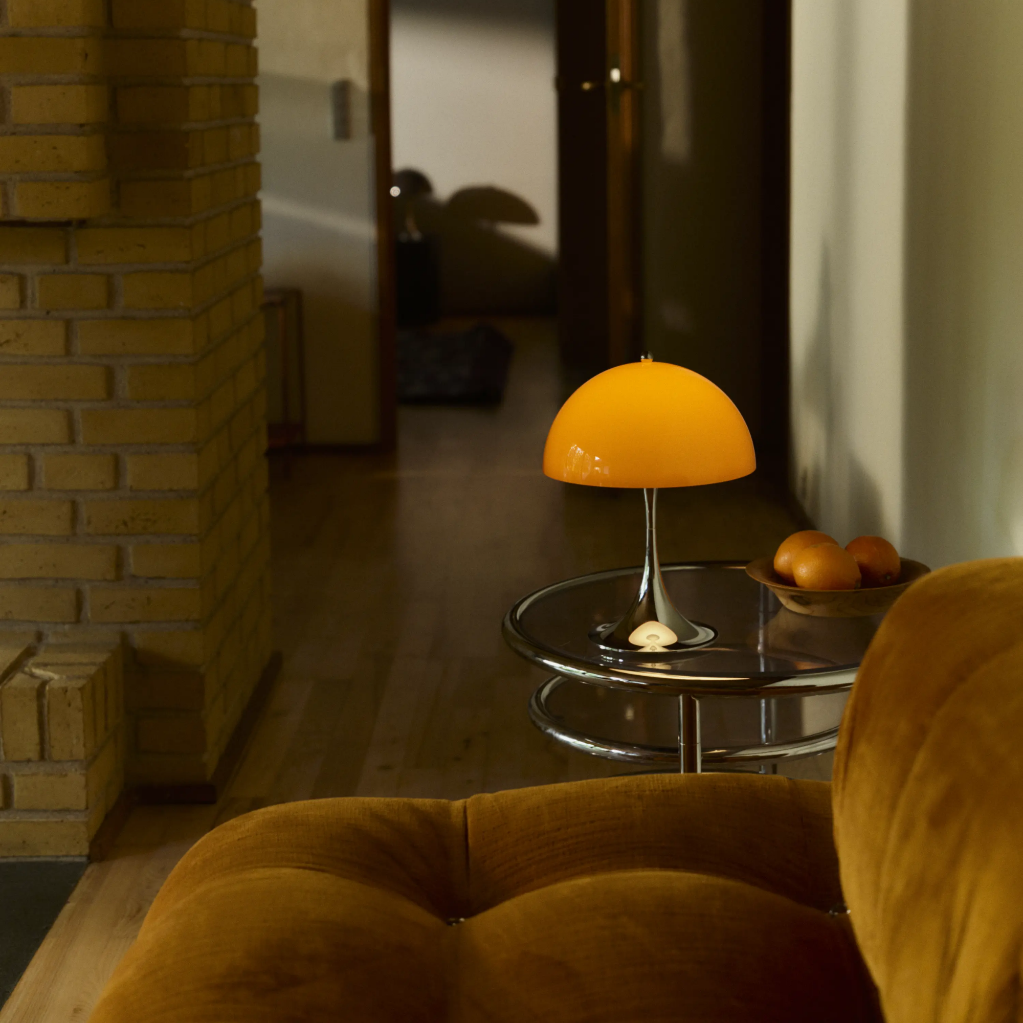 The 13.2 inch orange Panthella Portable Lamp: The Originals from Louis Poulsen in a lounge on top of a table beside a couch.