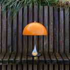 The 13.2 inch orange Panthella Portable Lamp: The Originals from Louis Poulsen in an outdoor terrace on a bench beside plants.