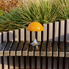 The 9.5 inch orange Panthella Portable Lamp: The Originals from Louis Poulsen in a garden.
