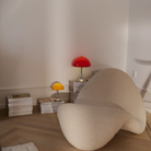 The 9.5 inch orange Panthella Portable Lamp: The Originals from Louis Poulsen in a lounge beside a chair and reading materials.