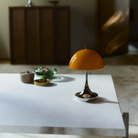 The 9.5 inch orange Panthella Portable Lamp: The Originals from Louis Poulsen in a primary bedroom on top of an accent table.