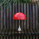 The 13.2 inch red Panthella Portable Lamp: The Originals from Louis Poulsen in a garden on top of a bench.