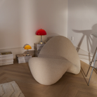 The 13.2 inch red Panthella Portable Lamp: The Originals from Louis Poulsen in a living room on top of a stack of magazines beside a lounge chair.