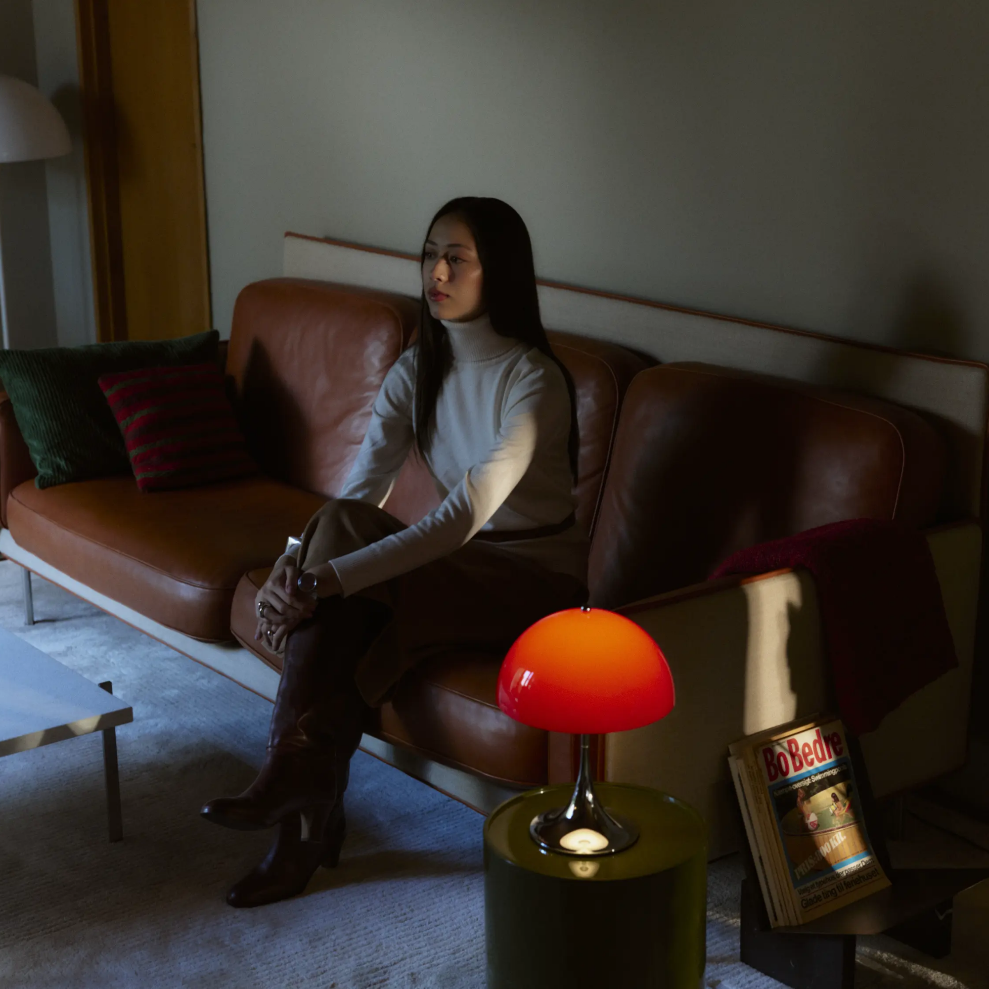 The 13.2 inch red Panthella Portable Lamp: The Originals from Louis Poulsen in a living space beside a woman on a couch.