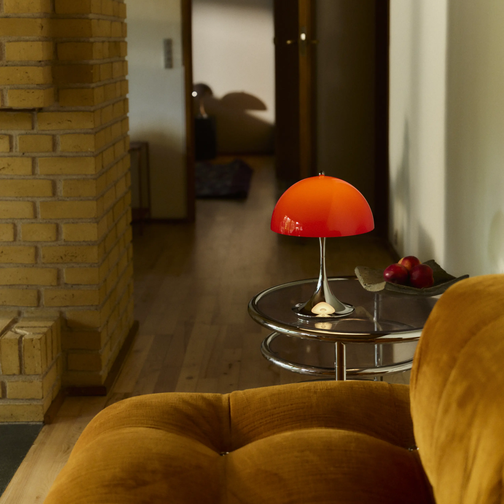 The 13.2 inch red Panthella Portable Lamp: The Originals from Louis Poulsen in a lounge beside a sofa on a table.