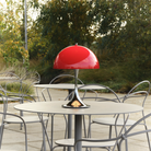 The 13.2 inch red Panthella Portable Lamp: The Originals from Louis Poulsen in an outdoor dining area on top of a table.