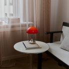 The 9.5 inch red Panthella Portable Lamp: The Originals from Louis Poulsen in a living room beside a bench.