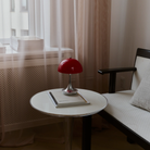 The 9.5 inch red Panthella Portable Lamp: The Originals from Louis Poulsen in a living space next to a sofa on top of a table beside a window.