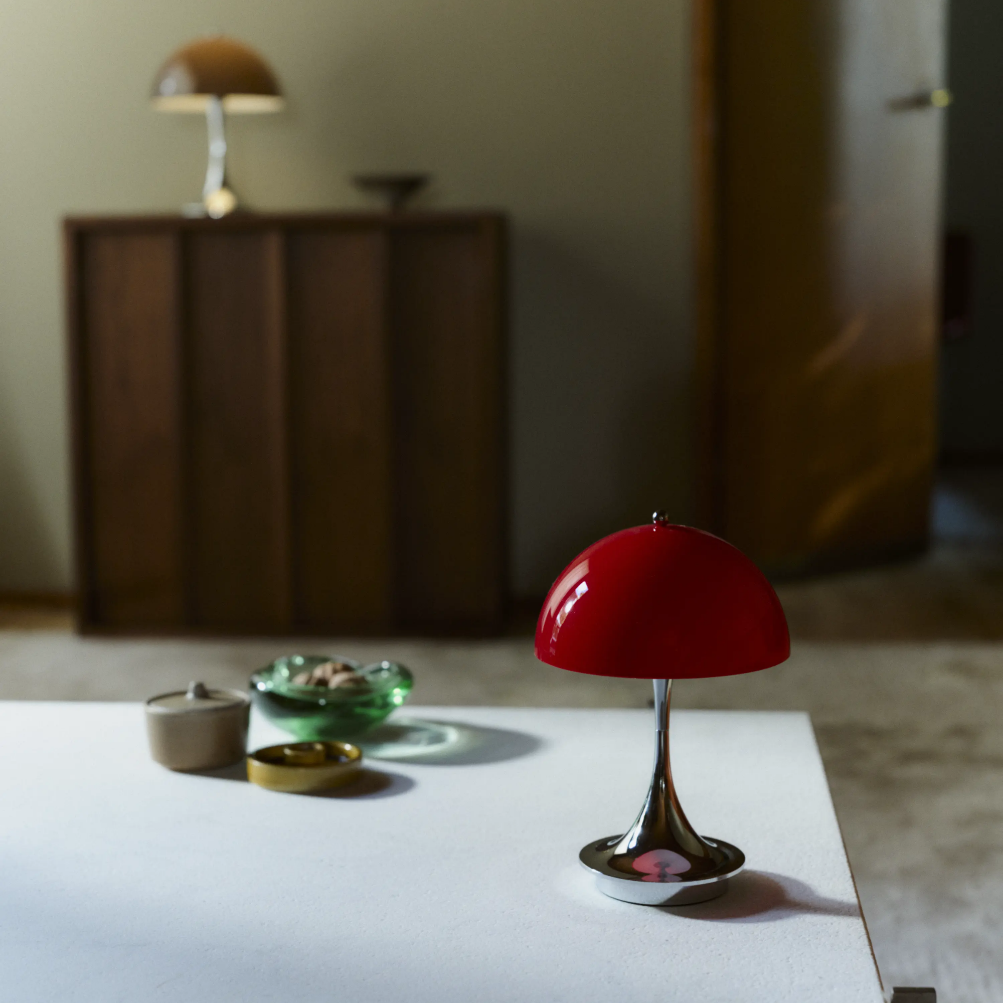 The 9.5 inch red Panthella Portable Lamp: The Originals from Louis Poulsen in a primary bedroom on top of a coffee table.