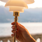 The brass PH 1/1 Portable Lamp from Louis Poulsen held in an outdoor terrace with the back drop of a lake.