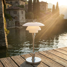 The chrome PH 1/1 Portable Lamp from Louis Poulsen on a dock next to an Italian lake.