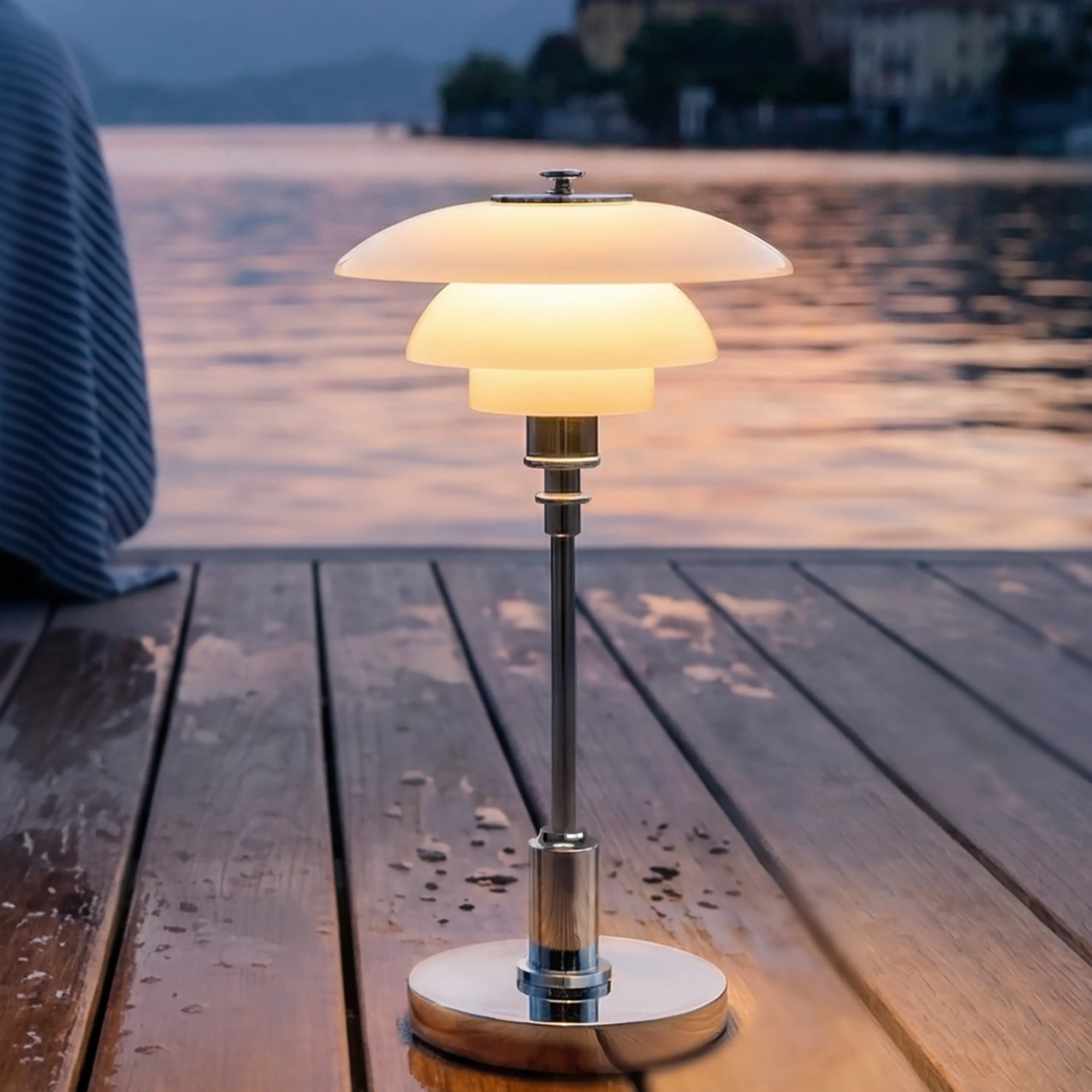 The chrome PH 1/1 Portable Lamp from Louis Poulsen used on a pier beside a lake to illuminate the night.