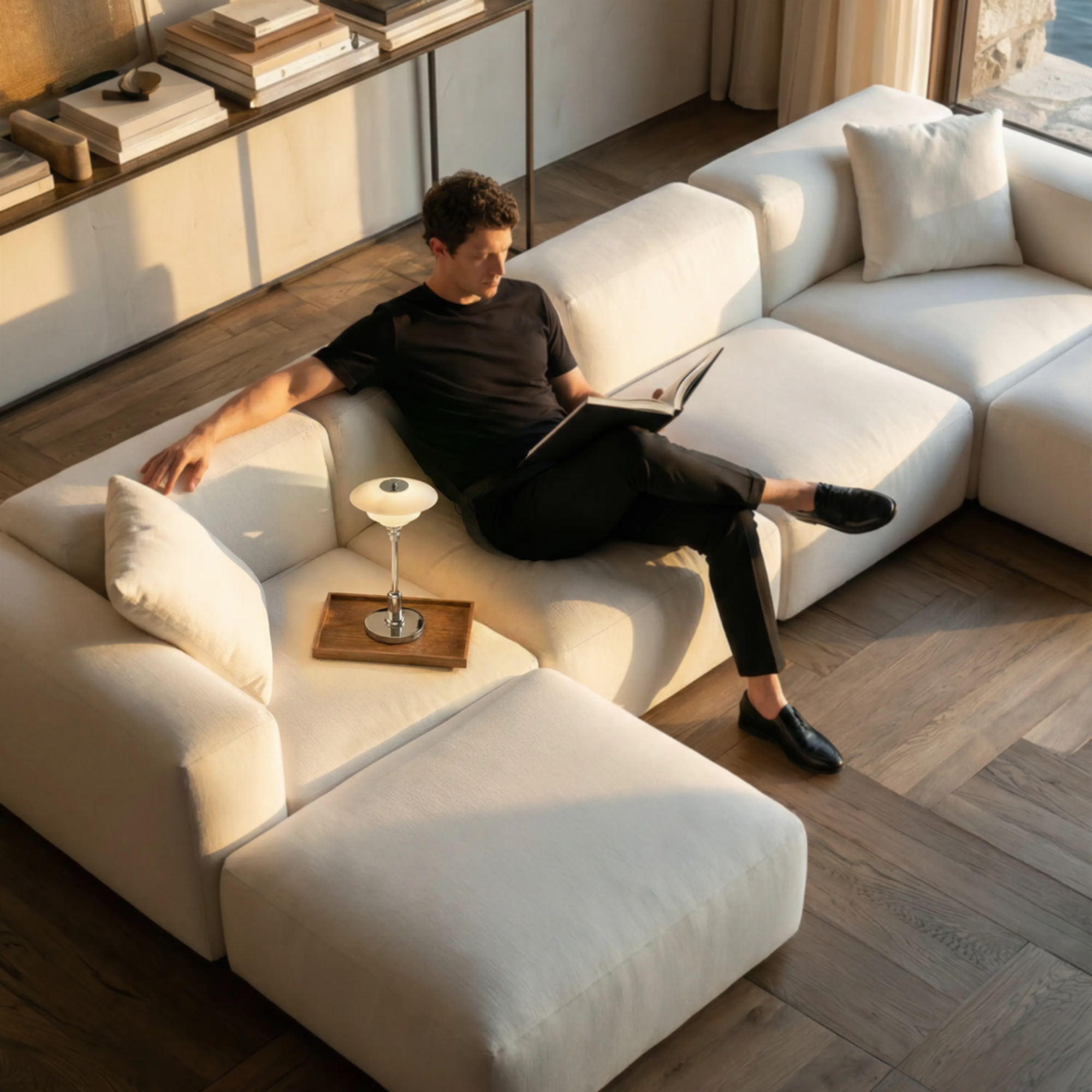 The chrome PH 1/1 Portable Lamp from Louis Poulsen in a lounge on a sofa with a man reading a book.