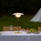 The brass PH 2/1 Portable Lamp from Louis Poulsen on an outdoor dining table beside grapes and peaches on dishes.