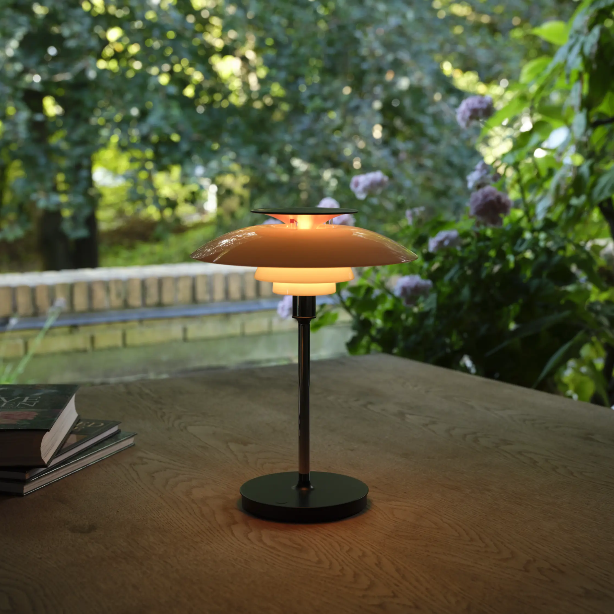 The opal white and high luster chrome plate PH 80 Portable Lamp from Louis Poulsen in an outdoor lounge on top of a table.