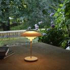 The opal white and white plate PH 80 Portable Lamp from Louis Poulsen on a table in an outdoor terrace overlooking a garden.
