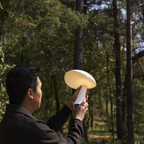 The cloud white Rumee 220 Portable Lamp from Louis Poulsen handheld in a forest.
