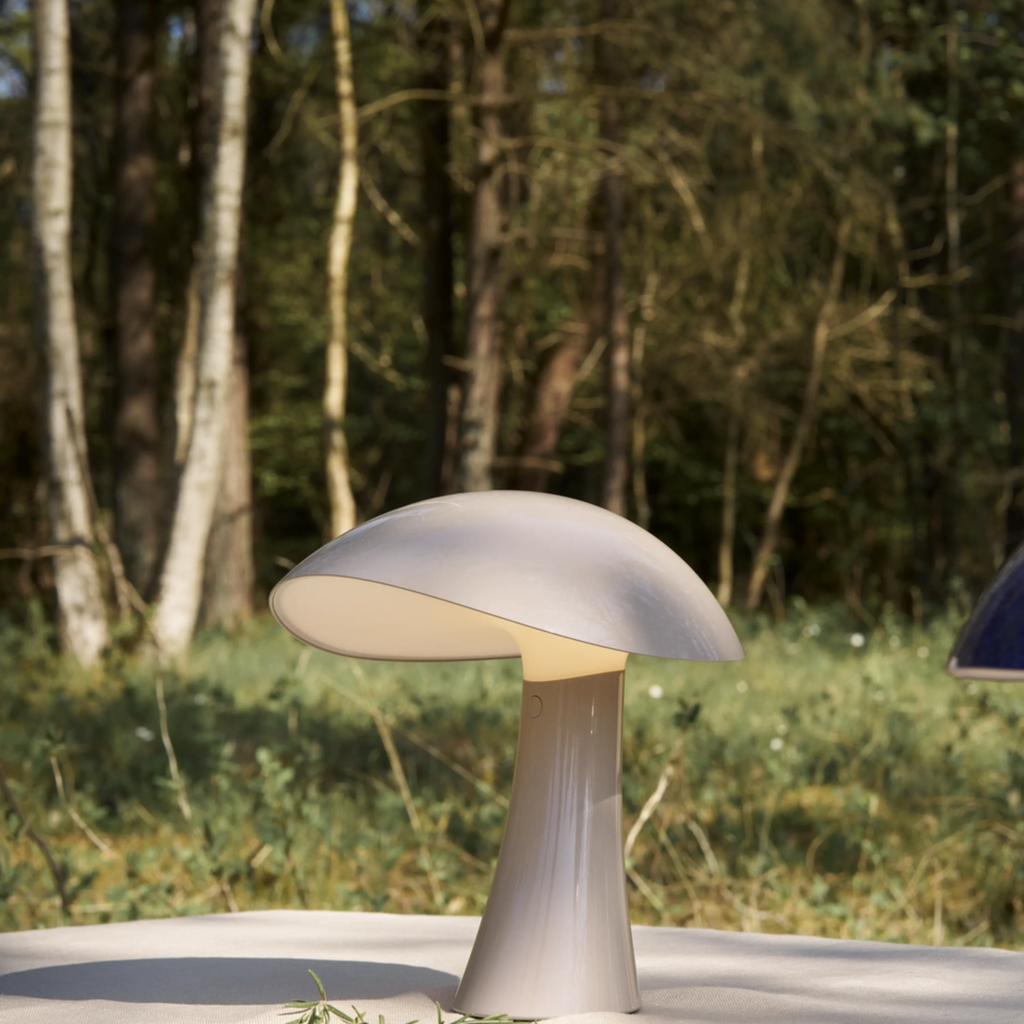 The earth gray Rumee 220 Portable Lamp from Louis Poulsen in a garden.