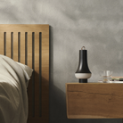 The dark brown Tomoshi Portable Lamp from Louis Poulsen in a designer bedroom beside the bed on a table.