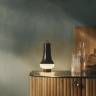 The dark brown Tomoshi Portable Lamp from Louis Poulsen in a lounge beside a drink set.