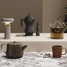 The gray Ease Cordless Lamp from Muuto in a kitchen and dining setting beside coffee and tea appliances.