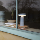 The light blue Ease Cordless Lamp from Muuto in a living room through a rainy window.