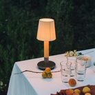 The Básica Mínima Batería Cordless Lamp from Santa & Cole with the natural ribbon shade used in an outdoor dining area.