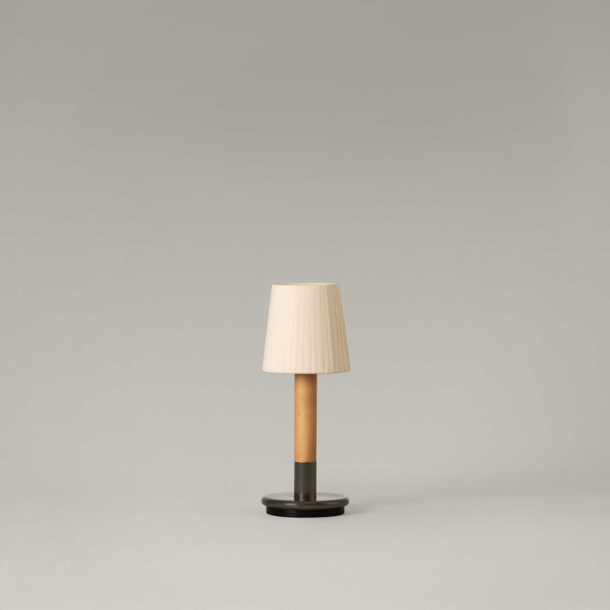 The Básica Mínima Batería Cordless Lamp from Santa & Cole with the natural ribbon shade turned off in a studio.