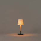 The Básica Mínima Batería Cordless Lamp from Santa & Cole with the natural ribbon shade turned on in a studio.