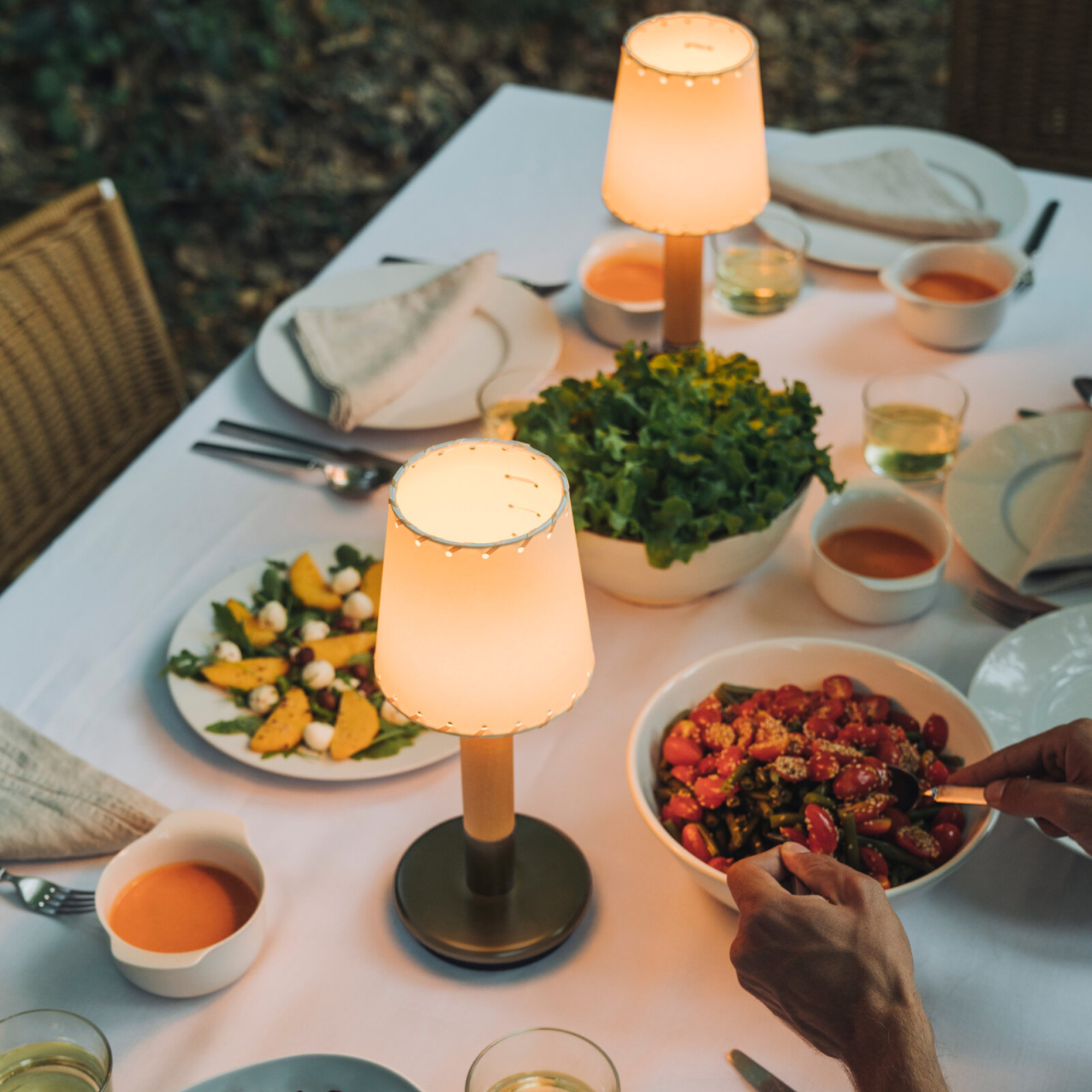 The Básica Mínima Batería Cordless Lamp from Santa & Cole with the stitched beige parchment shade being used for outdoor dining.