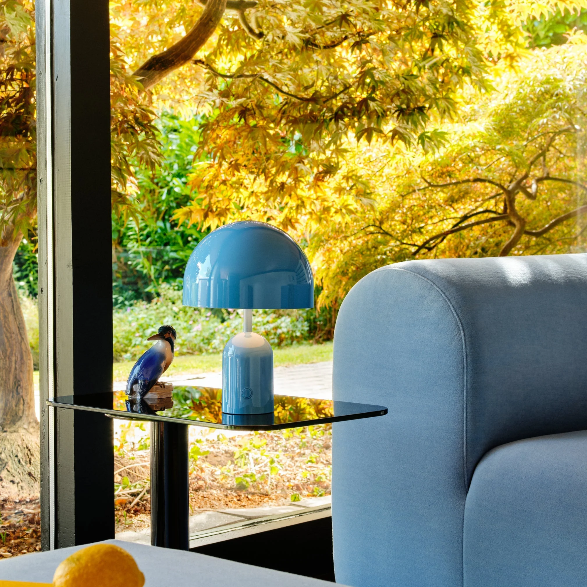 The baby blue Bell Cordless Lamp from Tom Dixon in a living room on an end table next to a sofa.
