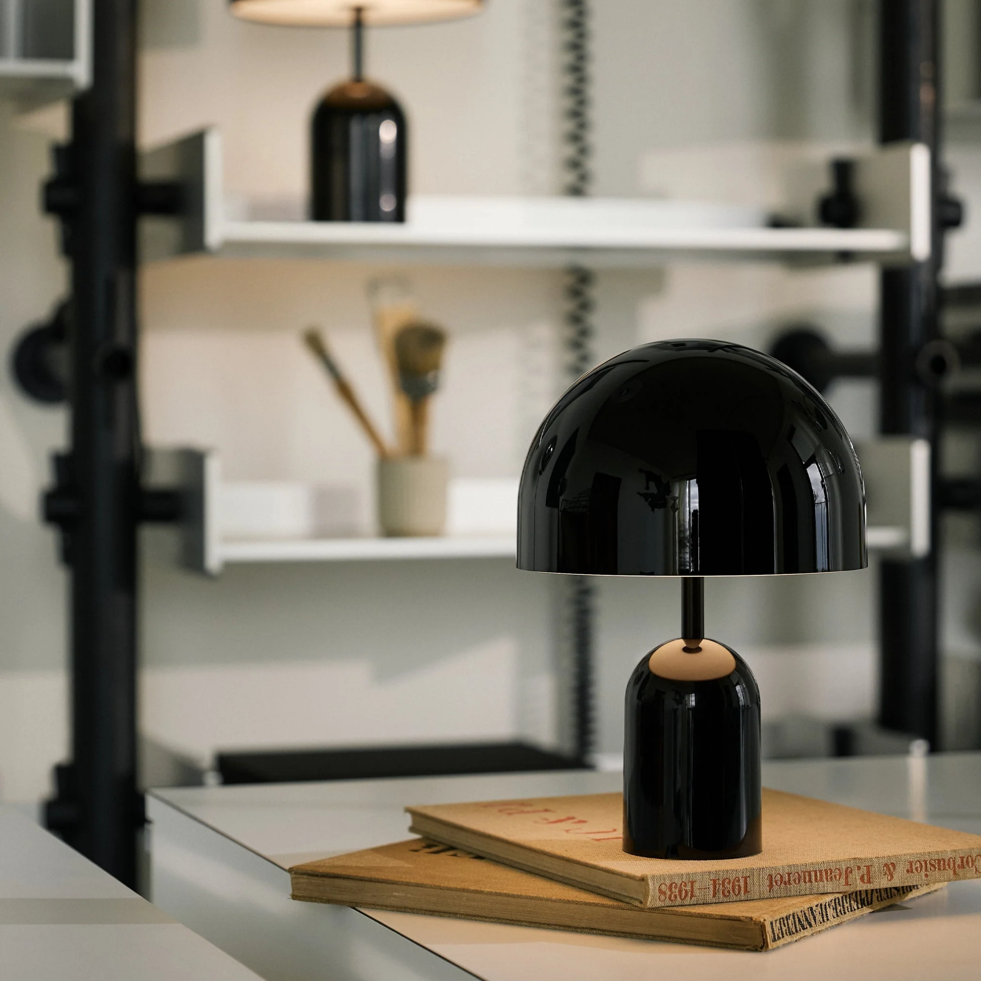 The black Bell Cordless Lamp from Tom Dixon in a home office in front of a bookshelf.