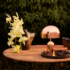 The copper Bell Cordless Lamp from Tom Dixon in an outdoor dining area on top of a table.