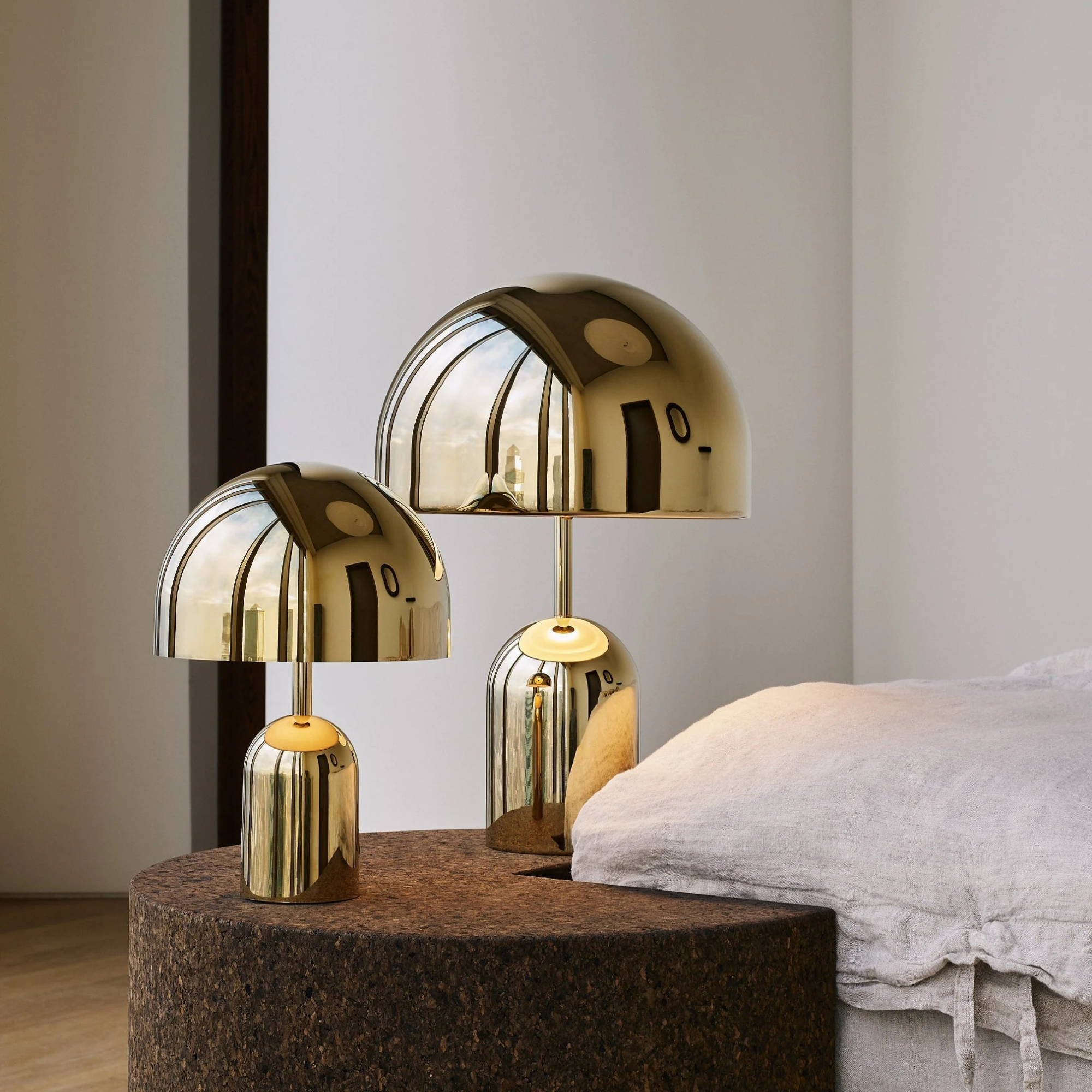 The gold Bell Cordless Lamp from Tom Dixon in a bedroom beside a bed.