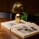The gold Bell Cordless Lamp from Tom Dixon in a lounge on top of a book on a table.