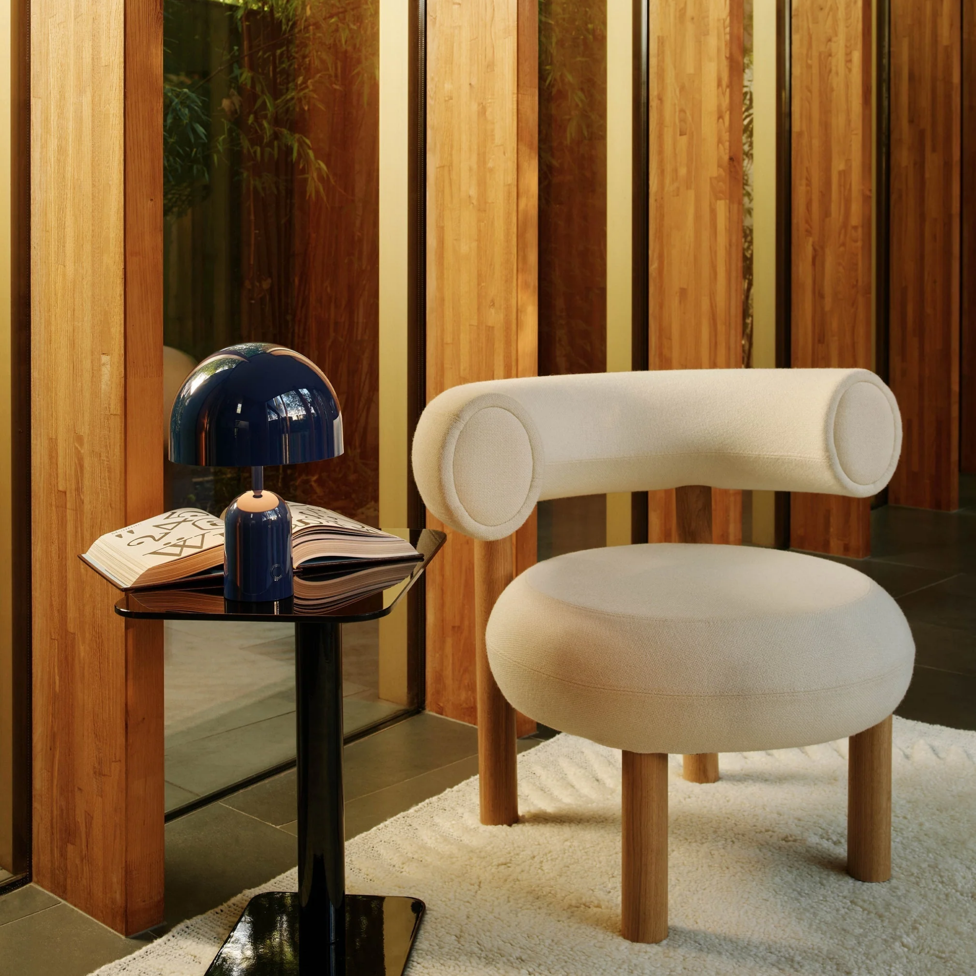 The indigo Bell Cordless Lamp from Tom Dixon shown in a lounge beside a lounge chair.