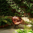 The copper Melt Cordless Floor Lamp from Tom Dixon in an outdoor living space surrounded by plants.