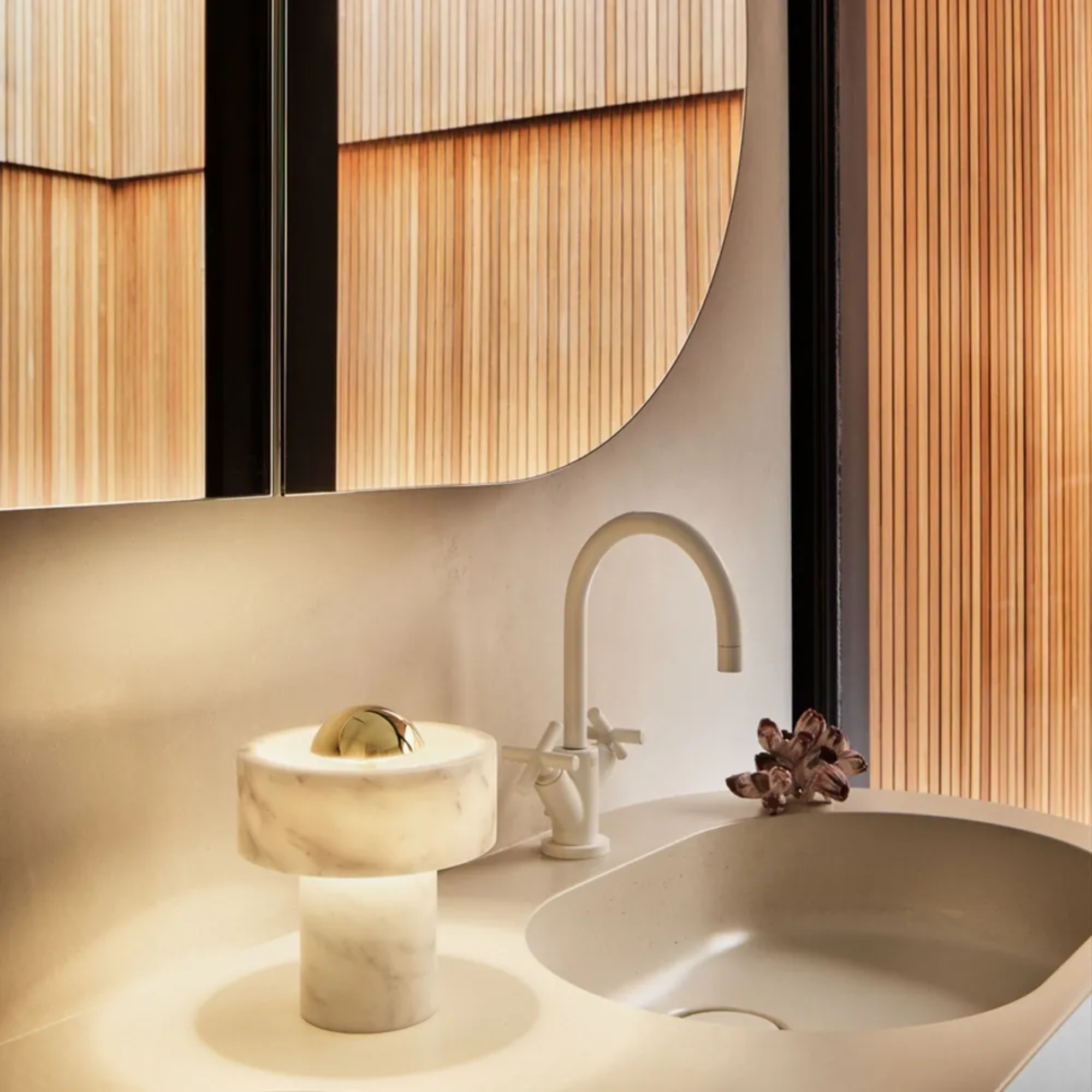 The gold Stone Cordless Lamp from Tom Dixon next to a bathroom sink, under a mirror.